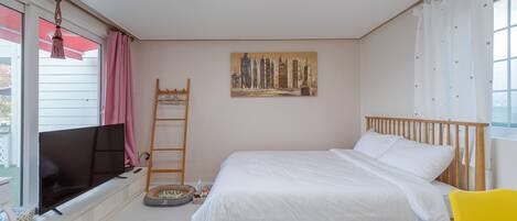 Un dormitorio con cama, televisor, un cuadro y ventana con cortinas.