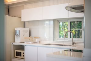 A modern kitchen with white cabinetry, a built-in microwave, a water dispenser, and a window with a view of greenery.