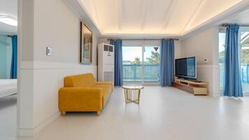 Uma sala de estar moderna com sofá, uma mesinha, televisão e varanda com cortinas azuis.