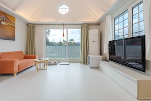 A modern living room with a sofa, a small round table, a TV, and a sliding glass door leading to a balcony.