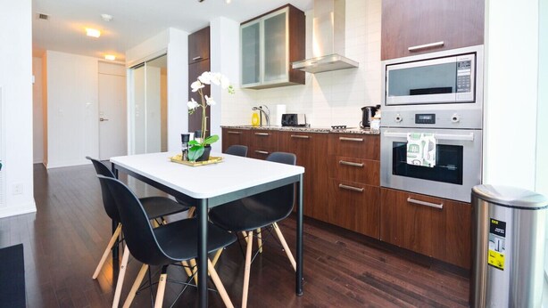 A modern kitchen with wooden cabinets, a microwave, an oven, and a dining area with a table and chairs.
