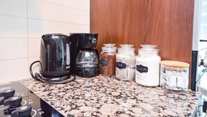 A kitchen counter with a coffee maker, a glass carafe, and jars labeled with ingredients like coffee, tea, sugar, and creamer.