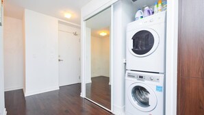 A laundry room with a stacked washer and dryer, a wooden floor, and a white door.