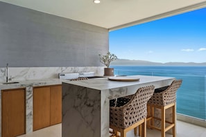 A modern kitchen with a marble countertop, wooden cabinets, and a view of the sea. - Beachfront Lux 3BR, 2 Pools + Rooftop | Panarea 7B (Bucerías)