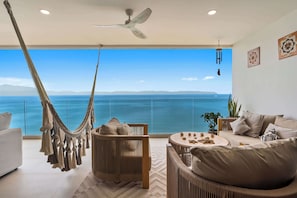 A modern living room with a hammock, a ceiling fan, and a view of the sea. - Beachfront Lux 3BR, 2 Pools + Rooftop | Panarea 7B (Bucerías)