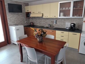 A modern kitchen with a wooden dining table, white chairs, a built-in oven, a coffee maker, and a sink.