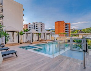 A rooftop pool area with lounge chairs, a glass railing, and a view of surrounding buildings. - Edificio Riomaggiore City Tower (Cali)