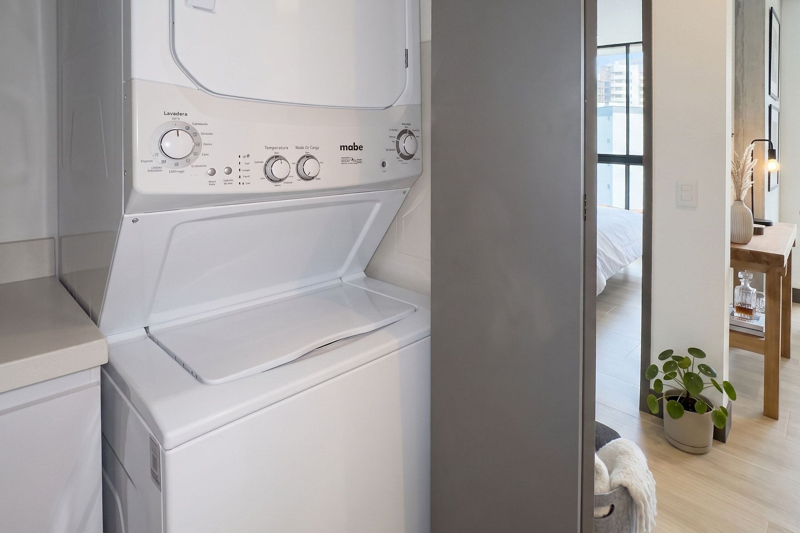 A modern laundry room with a front-loading washing machine, a drying rack, and a small potted plant.