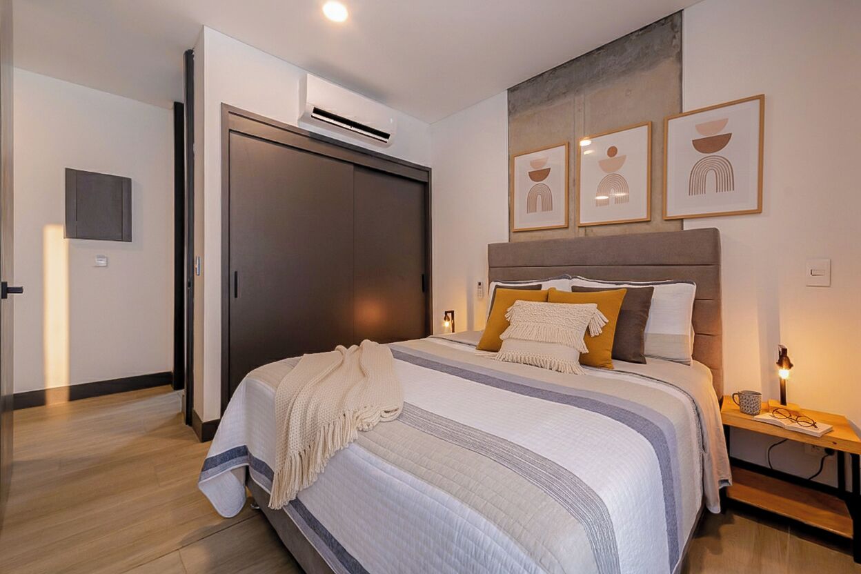 A bedroom with a bed, bedside table, wall art, and an air conditioning unit.