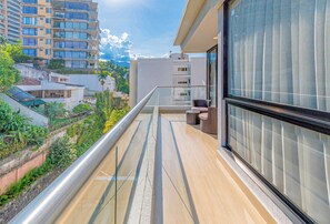 A balcony with a glass railing, a wicker chair, and a view of a cityscape. - Edificio Riomaggiore City Tower (Cali)