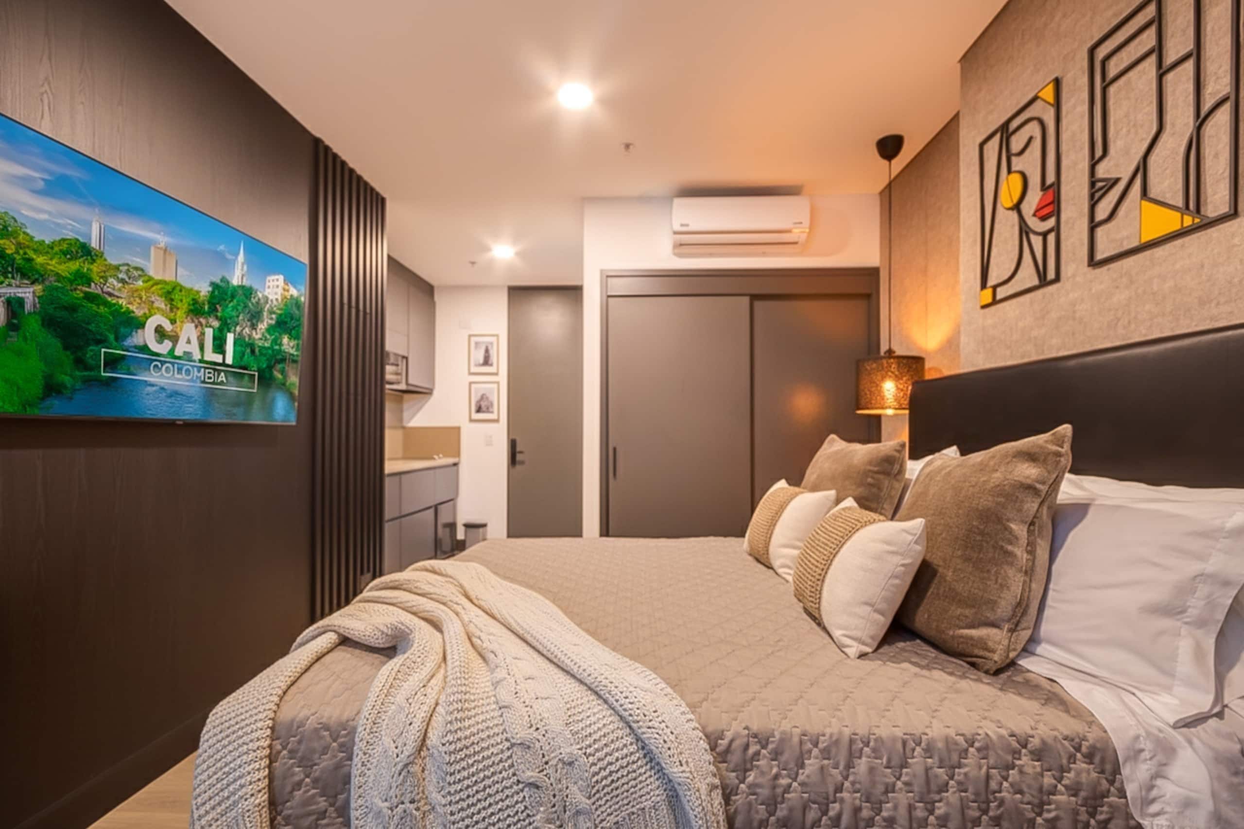 A modern bedroom with a large bed, a flat-screen TV on the wall, and a cityscape view.