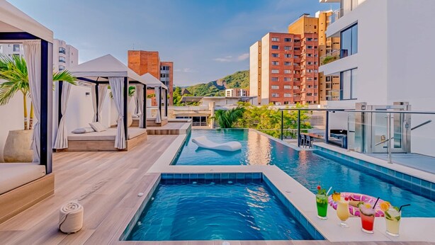 Une piscine sur le toit, dotée d’une balustrade en verre, un cabanon et un espace de détente offrant une vue sur le paysage urbain.