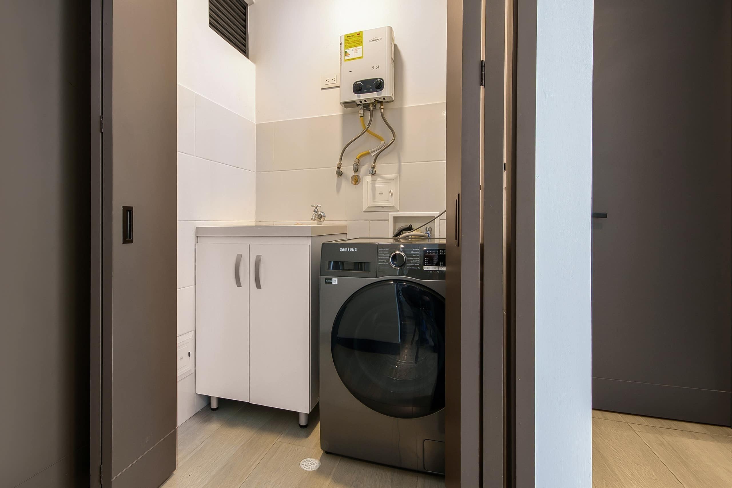 A compact laundry room with a washing machine, a small cabinet, and a water heater.