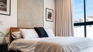 A hotel room with a large bed, a nightstand with a plant, and a window with a view of buildings. - Edificio Riomaggiore City Tower (Cali)