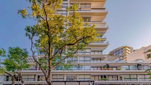 Un immeuble à plusieurs étages, doté de balcons, avec un arbre au premier plan.