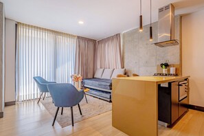 Una sala moderna con un sofá, dos sillones, una isla de cocina y un comedor.