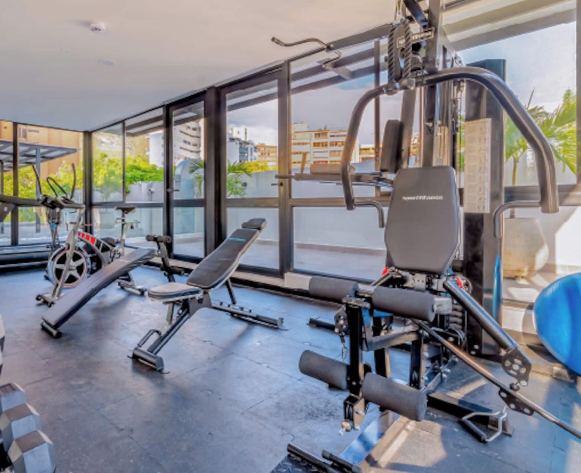 A gym with various exercise equipment, large windows, and a view of buildings and trees.