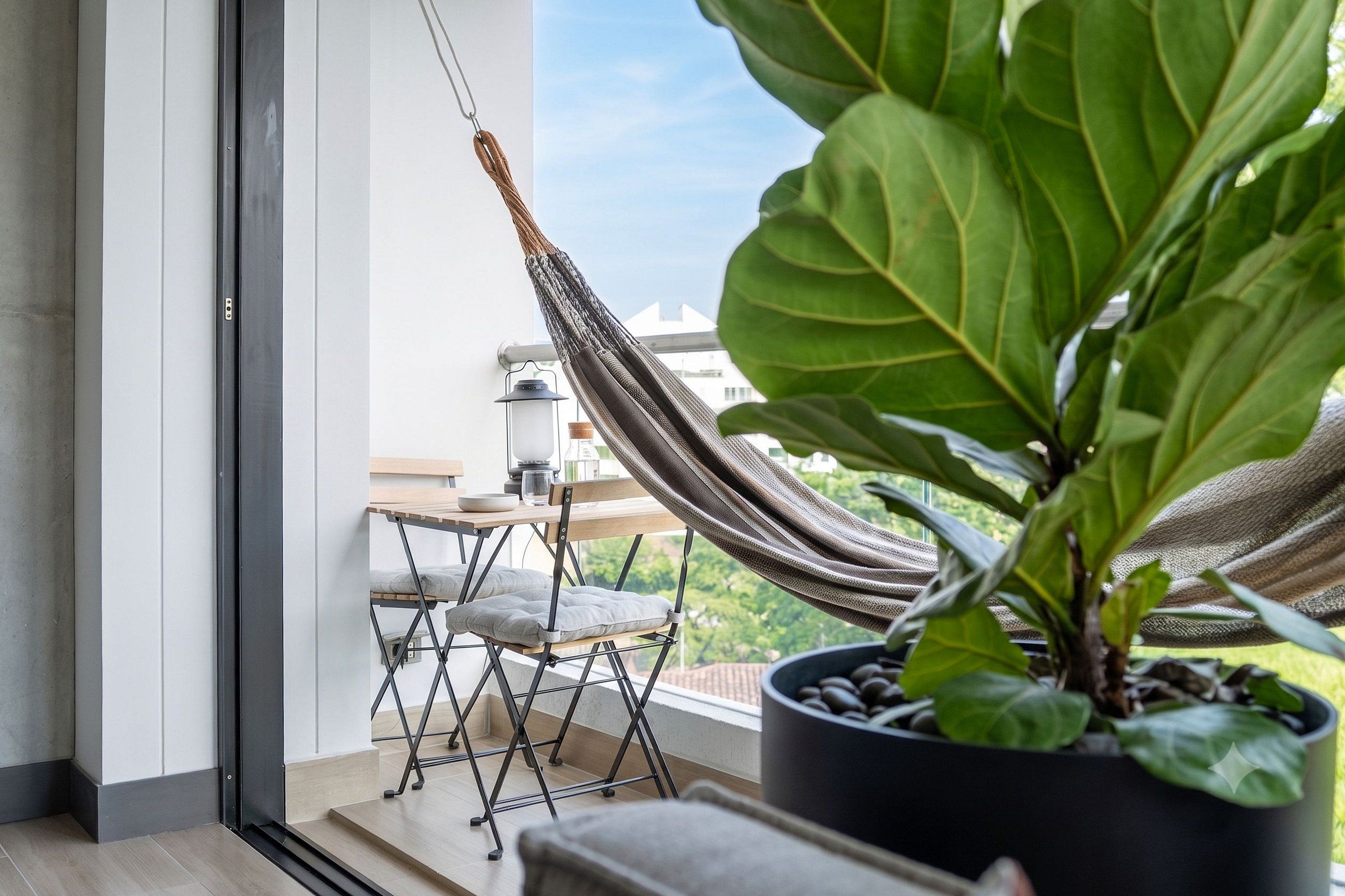 Ein Balkon mit einer Hängematte, einem Topfpflanzen und einem kleinen Tisch mit Stuhl.