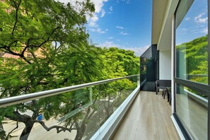 Uma varanda com guarda-corpo de vidro, vista para árvores e céu claro.