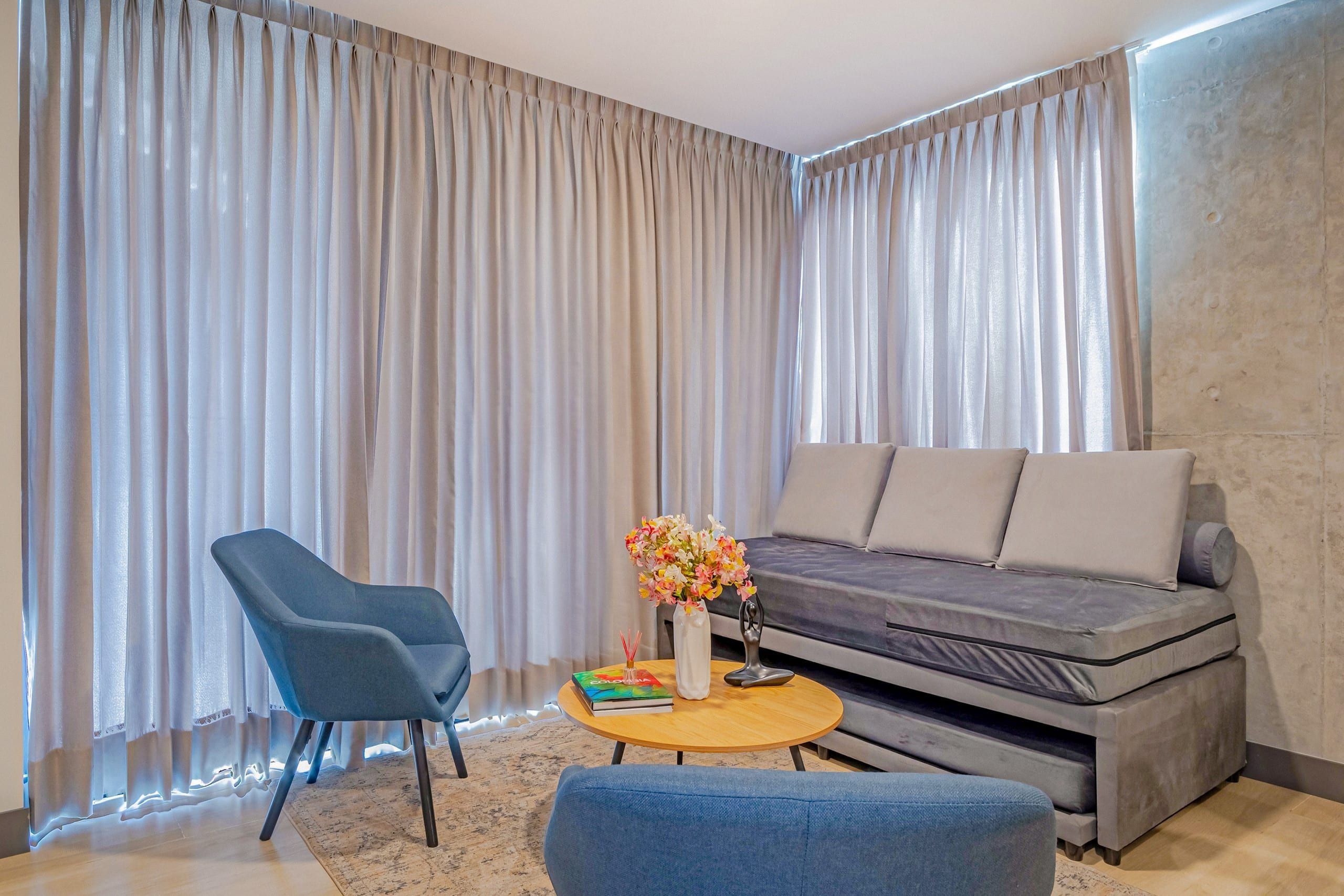 Uma sala de estar moderna com um sofá, uma poltrona azul, uma mesa de centro redonda e um vaso de flores.