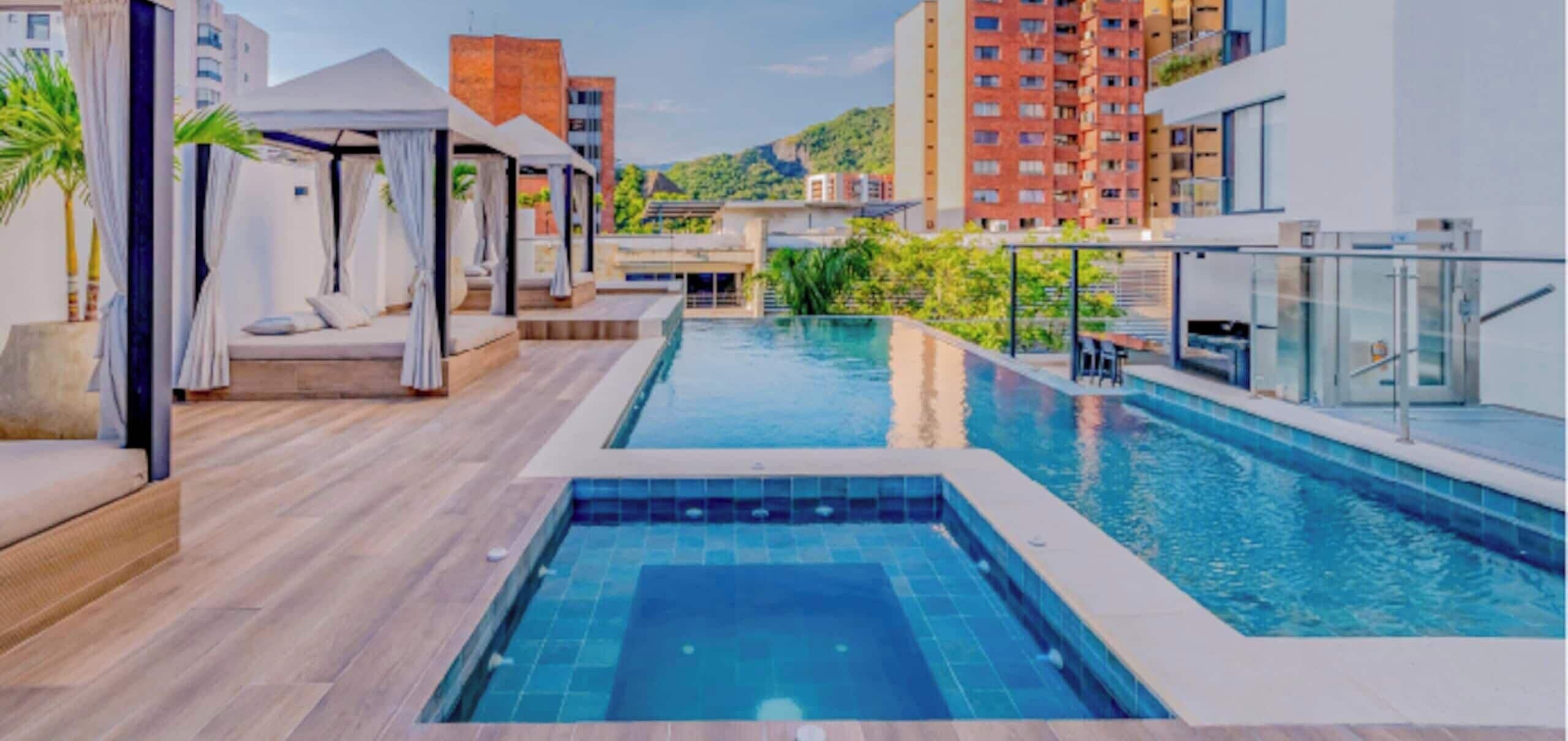 A rooftop pool area with a jacuzzi, lounge chairs, and a glass railing.