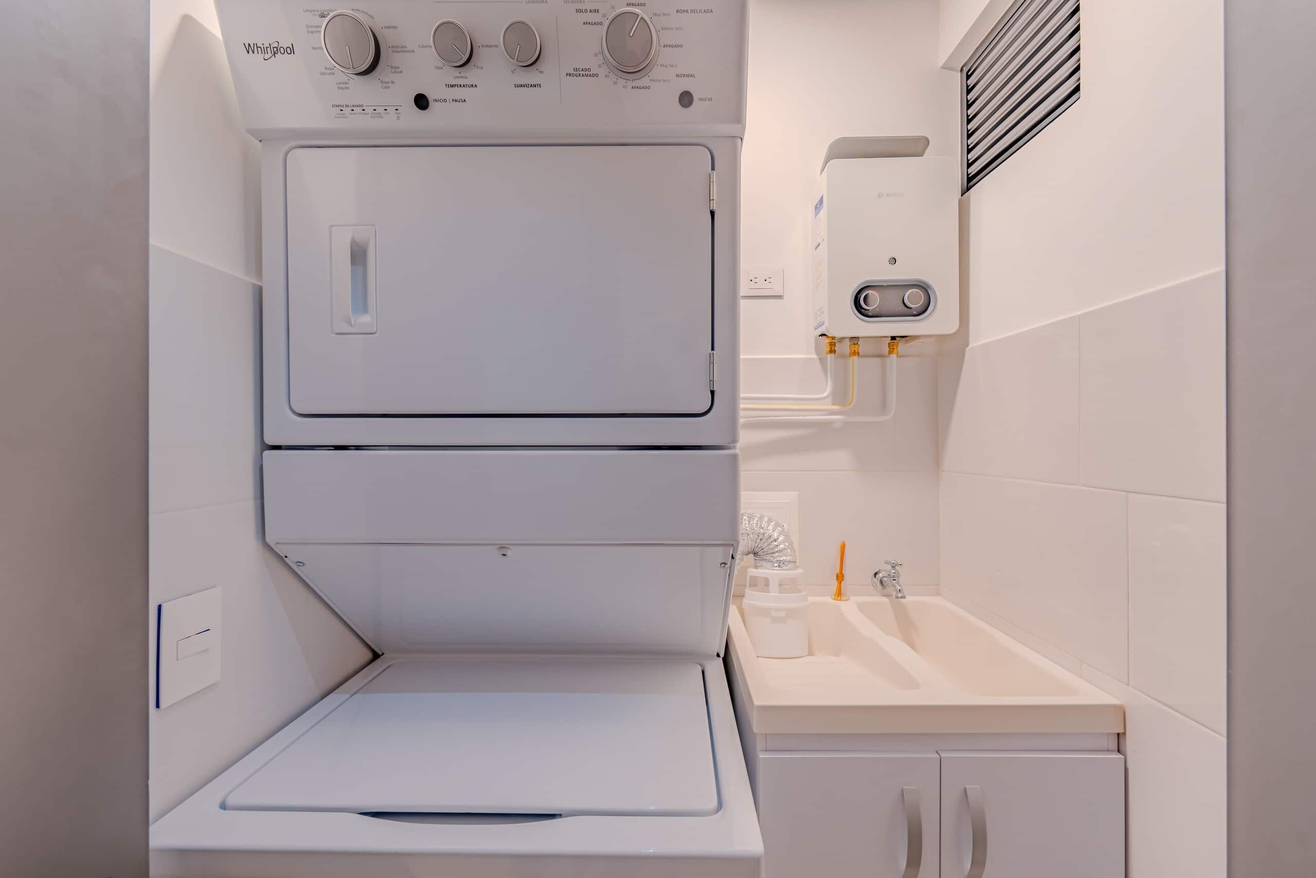 A compact laundry area with a stacked washer and dryer, a small countertop with a sink, and a vent above the dryer.