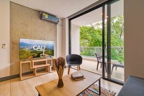 A modern living room with a flat-screen TV, wooden furniture, a vase, and a view of greenery through large windows. - Edificio Riomaggiore City Tower (Cali)