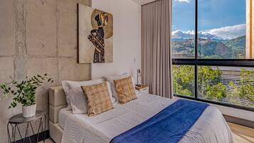 A modern bedroom with a large bed, a view of a cityscape, and a piece of abstract art on the wall.