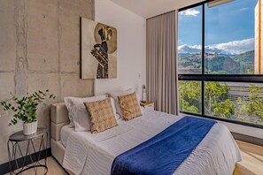 A modern bedroom with a large bed, a view of a cityscape, and a piece of abstract art on the wall. - Edificio Riomaggiore City Tower (Cali)