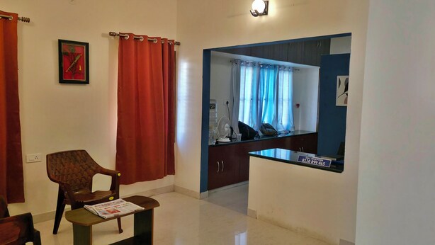 A room with a wooden chair, a table with a magazine, a reception desk, and a mirror reflecting a bathroom.