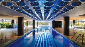 A swimming pool with a modern design, surrounded by large pillars and a view of greenery outside. - Luxe 2 Bed Apt, Seconds to Beach & Minutes to City (Port Melbourne)