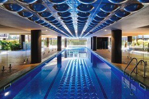 A swimming pool with a modern design, surrounded by large pillars and a view of greenery outside. - Luxe 2 Bed Apt, Seconds to Beach & Minutes to City (Port Melbourne)