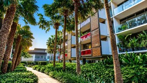 A modern building with multiple balconies, surrounded by palm trees and lush greenery. - Luxe 2 Bed Apt, Seconds to Beach & Minutes to City (Port Melbourne)