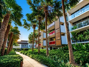 A modern building with multiple balconies, surrounded by palm trees and lush greenery. - Luxe 2 Bed Apt, Seconds to Beach & Minutes to City (Port Melbourne)