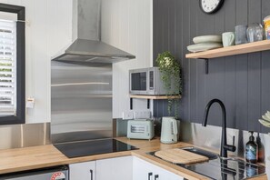 A modern kitchen with a stainless steel range hood, a microwave, a toaster, a kettle, and a sink with a black faucet. - Airport Studio Retreat (Midway Point)