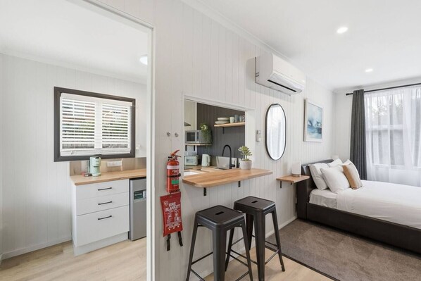 A modern bedroom with a bed, bedside table, and a window with curtains. - Airport Studio Retreat (Midway Point)