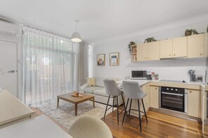 A compact living space with a kitchenette, a dining area with a table and chairs, and a sofa. - Courtyard 1-Bed Apartment in New Farm (New Farm)