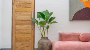 A wooden door, a potted plant, and a pink sofa in a room with a gray floor. - Kutesa Villa Bali (Kerobokan)