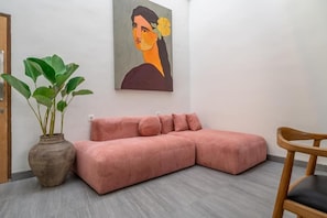 Uma sala de estar moderna com um sofá rosa, uma cadeira de madeira, uma planta em vaso e um quadro na parede.