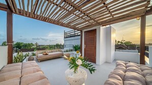 A rooftop terrace with a wooden pergola, cushioned seating, a decorative planter, and a view of the cityscape. - Kutesa Villa Bali (Kerobokan)