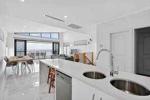 A modern kitchen with a large island, stainless steel sinks, and a dining area with a view. - 35A Franklin Pde Encounter Bay (Encounter Bay)
