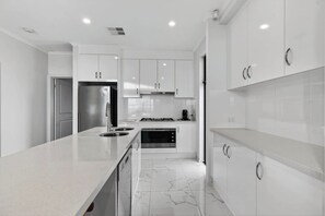 A modern kitchen with white cabinetry, a stainless steel refrigerator, a built-in oven, and a marble-tiled floor. - 35A Franklin Pde Encounter Bay (Encounter Bay)