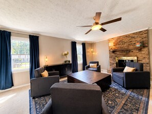 A modern living room with a fireplace, dark furniture, and a ceiling fan. - THE OWL POST - Pool, Games & Cinema Room (Columbus)