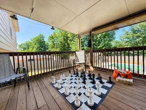 A wooden deck with a chessboard, outdoor seating, and a view of a swimming pool. - THE OWL POST - Pool, Games & Cinema Room (Columbus)