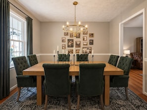 A dining room with a wooden table, green upholstered chairs, a chandelier, and framed pictures on the wall. - THE OWL POST - Pool, Games & Cinema Room (Columbus)
