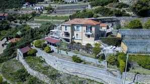 Rinteeseen rakennettu asuinalue, jossa on kaksikerroksinen talo, jonka punatiilikatolla, parvekkeella ja pienellä, erillisellä, punakattoisella lisärakennuksella on.