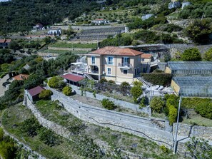 Eine Wohngegend an einer Hügelkuppe mit einem zweistöckigen Haus, das ein rotes Ziegeldach, einen Balkon und einen kleinen Anbau mit rotem Dach hat.
