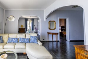 Ein modernes Wohnzimmer mit einer Couch, einem Essbereich mit Tisch und Stühlen sowie einem Flur, der in ein weiteres Zimmer führt.