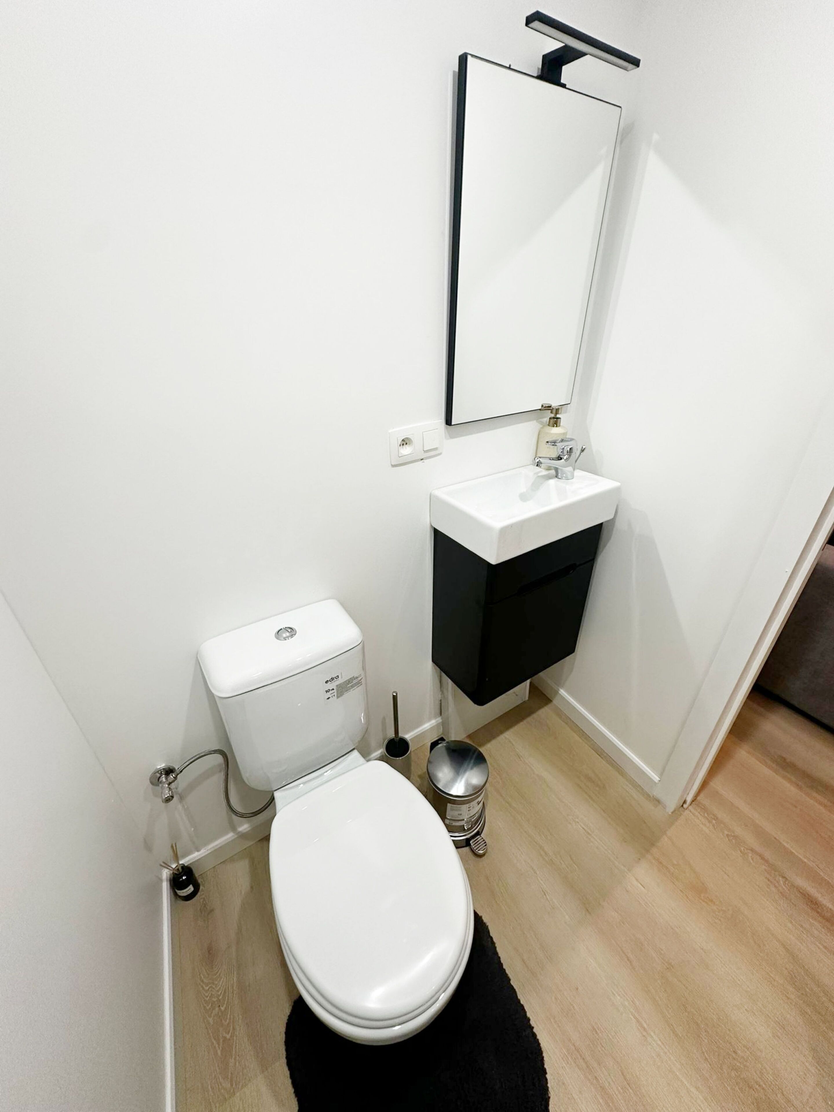 Een compacte, moderne badkamer met een wit toilet, een witte wastafel en een spiegel boven de wastafel.