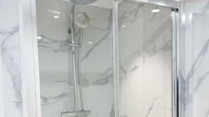 Une cabine de douche moderne dotée d’une porte en verre et d’un mur imitant le marbre.